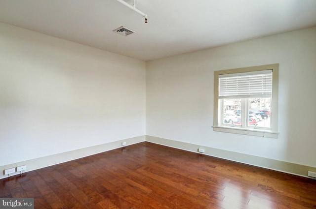 empty room with baseboards, visible vents, and dark wood finished floors