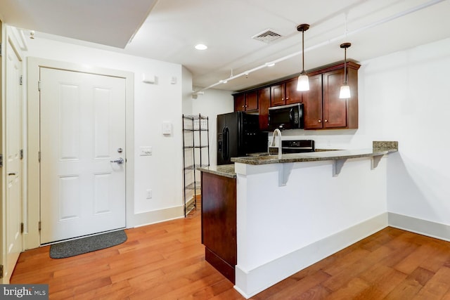 kitchen with visible vents, light wood-style flooring, a breakfast bar, a peninsula, and black appliances