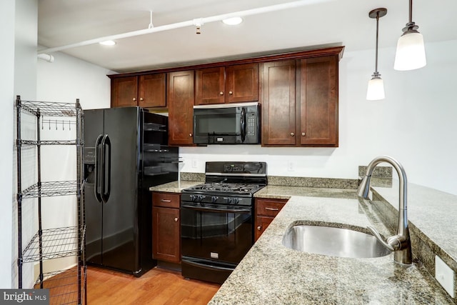 kitchen featuring light stone counters, hanging light fixtures, light wood-style floors, a sink, and black appliances