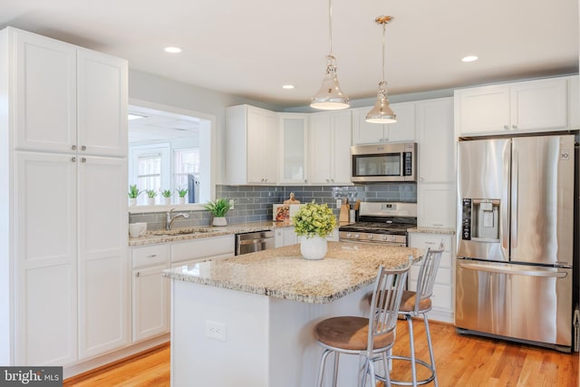 kitchen with stainless steel appliances, decorative backsplash, white cabinetry, a kitchen island, and light wood-type flooring