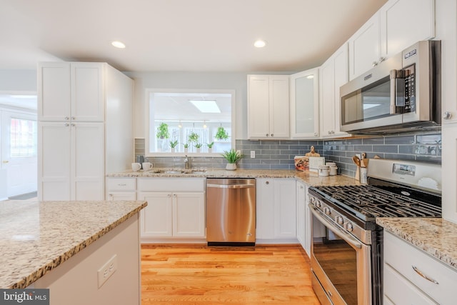 kitchen with stainless steel appliances, a sink, backsplash, and light wood finished floors