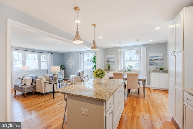 kitchen with light wood finished floors, a wealth of natural light, white cabinets, a kitchen island, and a kitchen breakfast bar