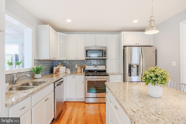 kitchen with decorative backsplash, light wood-style flooring, stainless steel appliances, white cabinetry, and a sink