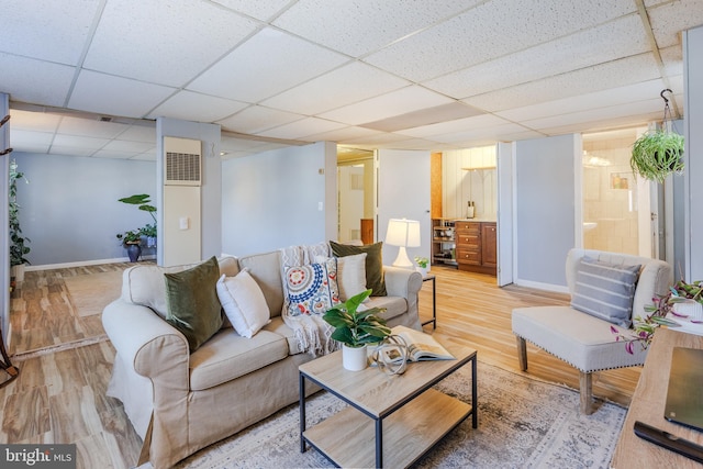 living area with light wood finished floors, a drop ceiling, visible vents, and baseboards