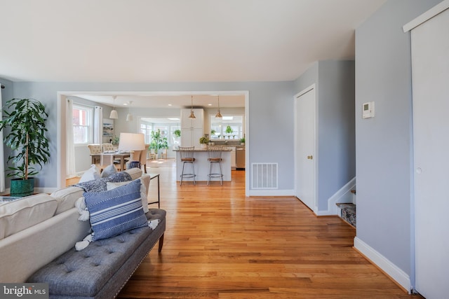 living area with baseboards, visible vents, stairway, and light wood finished floors