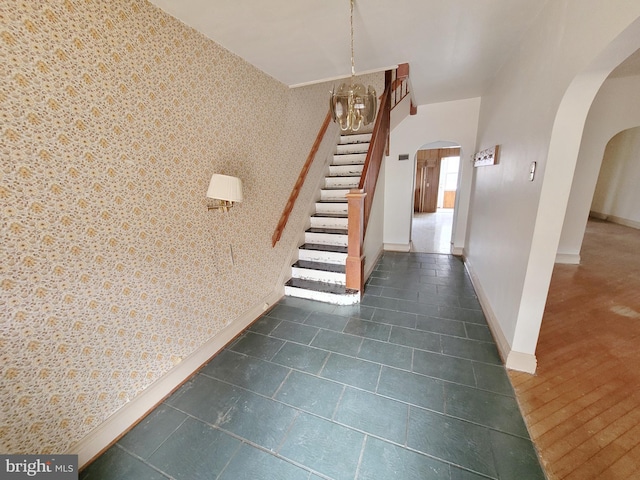 stairs featuring baseboards, arched walkways, an accent wall, and wallpapered walls