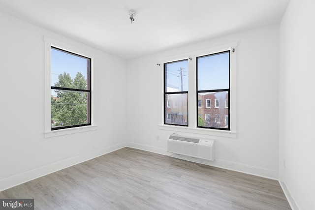 empty room featuring an AC wall unit, light wood-type flooring, and baseboards