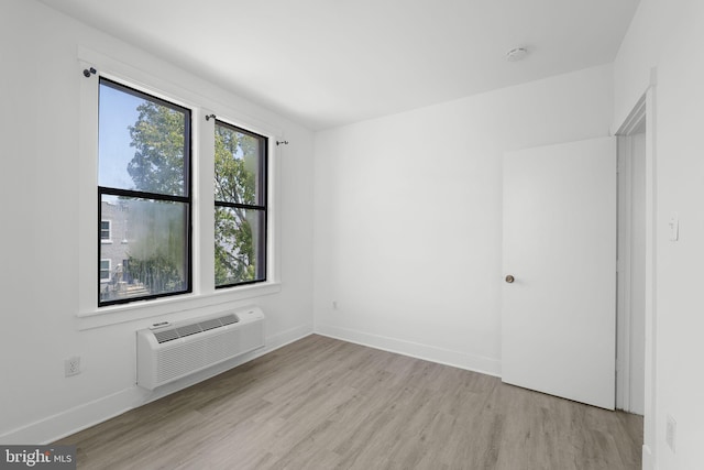 spare room featuring a wealth of natural light, a wall mounted air conditioner, baseboards, and wood finished floors