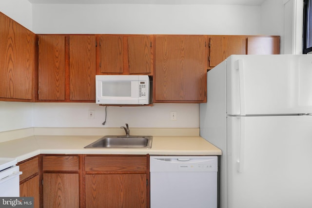 kitchen featuring brown cabinets, white appliances, light countertops, and a sink