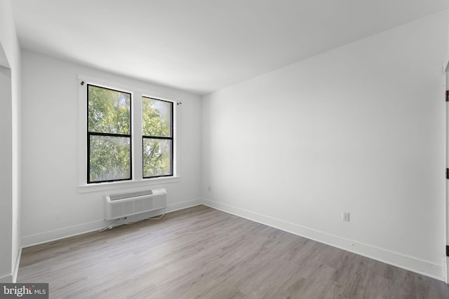 empty room with a wall unit AC, baseboards, and wood finished floors