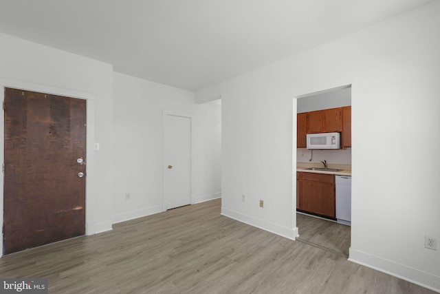 unfurnished living room featuring light wood finished floors, a sink, and baseboards