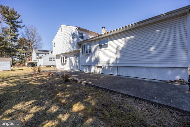 back of house with a patio area, a chimney, and a lawn