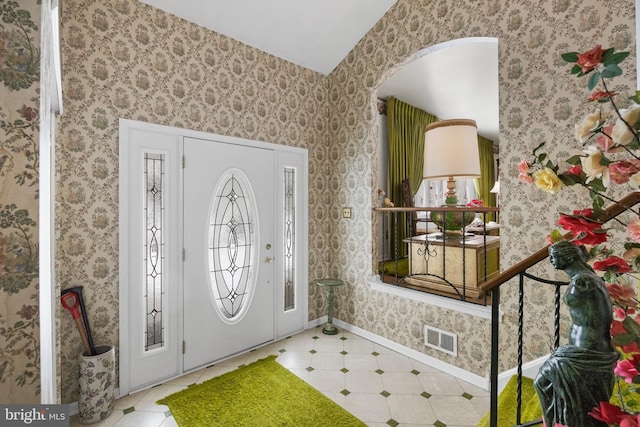 entryway with arched walkways, visible vents, baseboards, and wallpapered walls