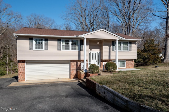 raised ranch with an attached garage, brick siding, a front yard, and aphalt driveway