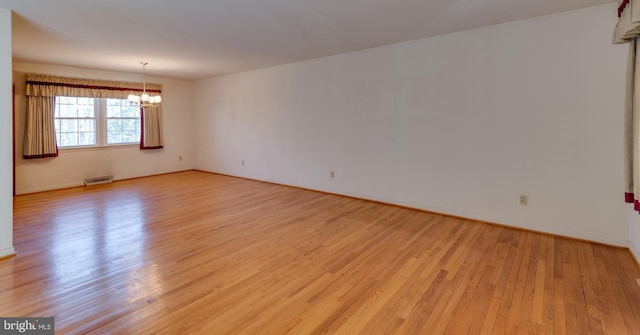 empty room with light wood finished floors, visible vents, and an inviting chandelier