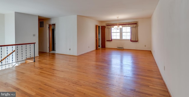 spare room with a chandelier, light wood-style flooring, visible vents, and baseboards