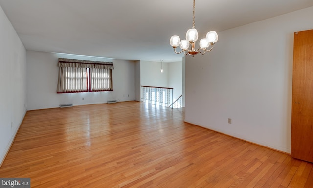 spare room with light wood-type flooring, visible vents, and a chandelier