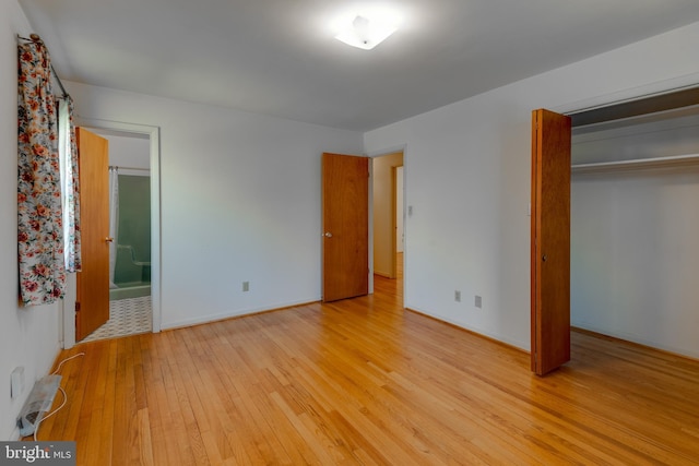 unfurnished bedroom with a closet, baseboards, ensuite bath, and light wood finished floors