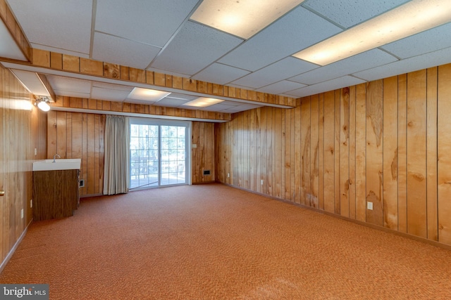 spare room featuring a drop ceiling, wood walls, carpet, and a sink