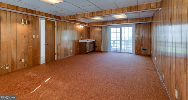 unfurnished room with carpet floors, wood walls, and a drop ceiling