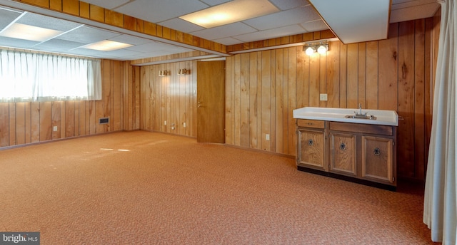 basement with a drop ceiling, wood walls, carpet, and a sink