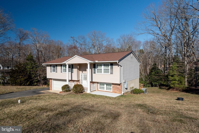 raised ranch featuring a garage, brick siding, driveway, and a front lawn