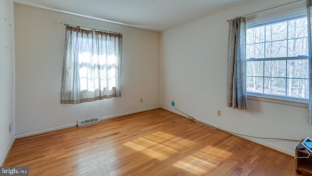 unfurnished room featuring wood-type flooring, visible vents, and baseboards