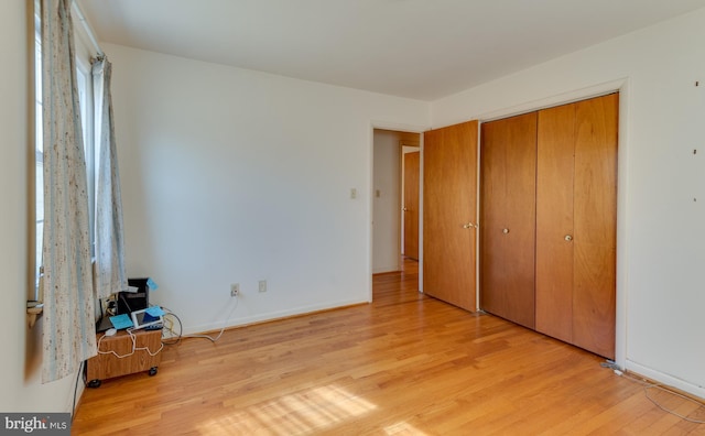 unfurnished bedroom featuring light wood-style flooring, baseboards, and a closet