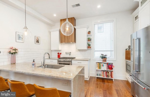 kitchen with visible vents, white cabinets, premium appliances, a peninsula, and a sink