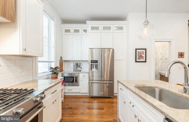 kitchen featuring light wood-style flooring, a sink, white cabinetry, hanging light fixtures, and appliances with stainless steel finishes