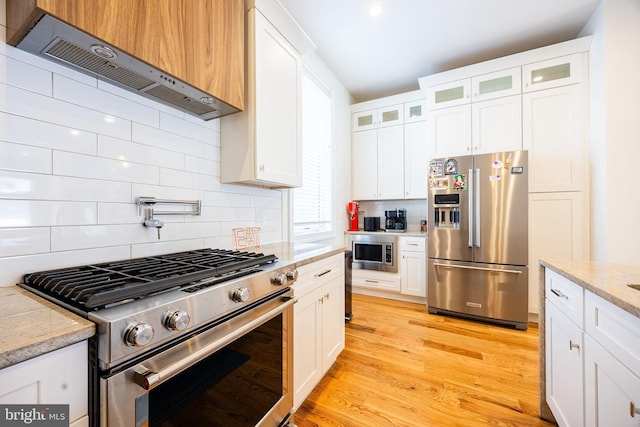 kitchen with light wood finished floors, wall chimney exhaust hood, appliances with stainless steel finishes, and decorative backsplash