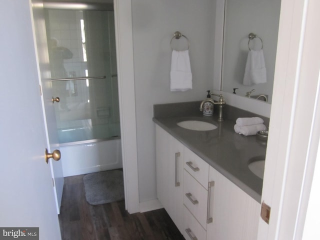 bathroom featuring a sink, double vanity, combined bath / shower with glass door, and wood finished floors