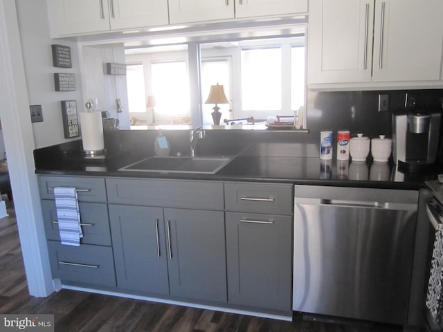 kitchen featuring dark wood finished floors, dark countertops, stainless steel dishwasher, white cabinets, and a sink