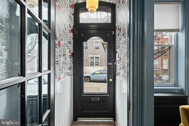 doorway featuring a wainscoted wall, tile walls, and wallpapered walls