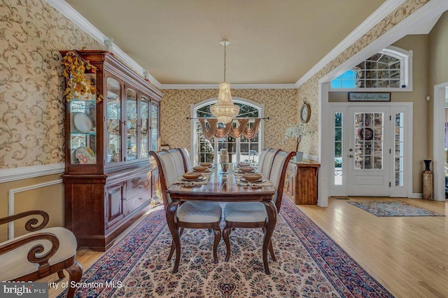 dining space featuring a notable chandelier, wood finished floors, ornamental molding, wainscoting, and wallpapered walls