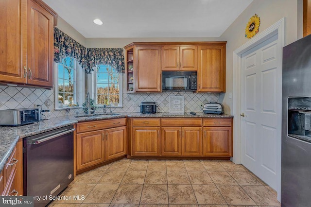 kitchen with light stone countertops, appliances with stainless steel finishes, brown cabinetry, and a sink