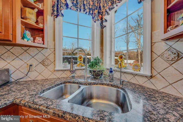 kitchen featuring brown cabinetry, dark stone counters, a sink, and tasteful backsplash