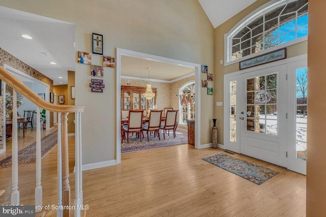 entrance foyer featuring high vaulted ceiling, wood finished floors, baseboards, ornamental molding, and wallpapered walls