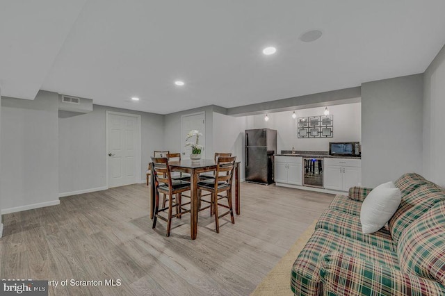 dining room with wet bar, beverage cooler, baseboards, and light wood finished floors