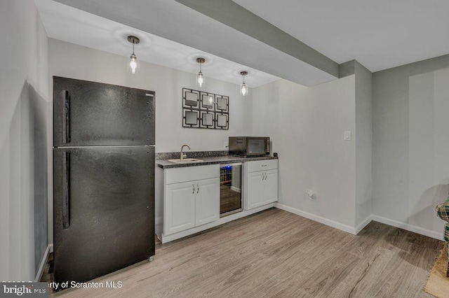 bar featuring wine cooler, light wood-style flooring, a sink, black appliances, and baseboards