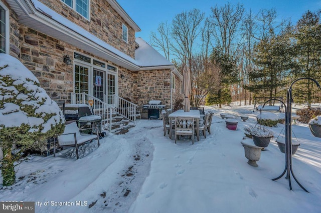 snow covered patio with entry steps, outdoor dining space, and grilling area