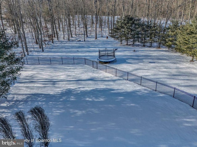 yard covered in snow with a trampoline and fence