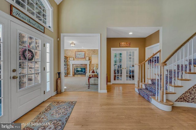 entryway with a glass covered fireplace, wood finished floors, stairs, a high ceiling, and french doors