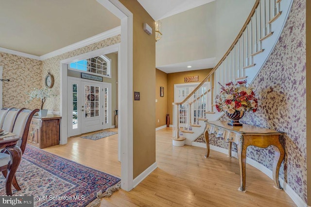 entryway with wallpapered walls, baseboards, hardwood / wood-style floors, a high ceiling, and crown molding