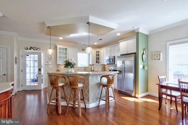 kitchen featuring dark wood-type flooring, a kitchen breakfast bar, stainless steel appliances, crown molding, and glass insert cabinets