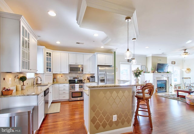 kitchen featuring a sink, open floor plan, stainless steel appliances, light wood finished floors, and light stone countertops