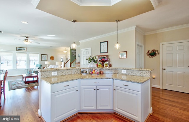 kitchen featuring crown molding, open floor plan, light wood-style flooring, hanging light fixtures, and white cabinets