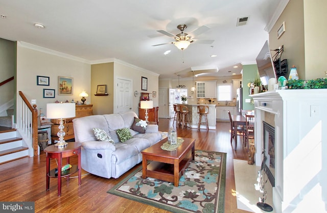 living area with visible vents, ornamental molding, wood finished floors, stairway, and a premium fireplace