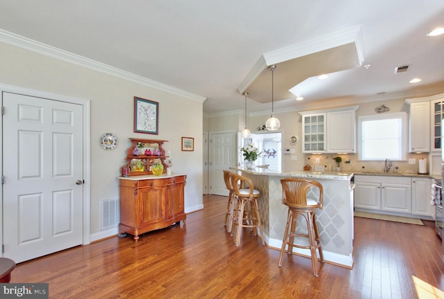 kitchen with a breakfast bar, glass insert cabinets, visible vents, and white cabinetry