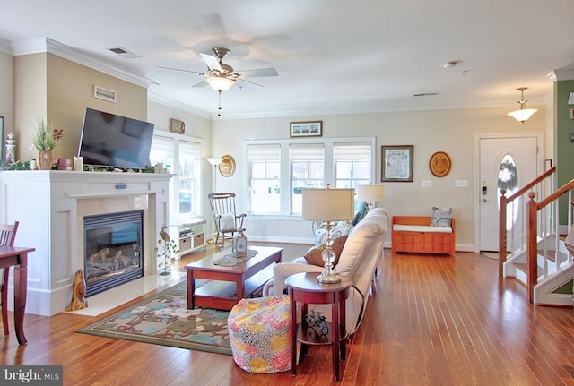 living room featuring visible vents, a fireplace, ornamental molding, stairs, and hardwood / wood-style flooring